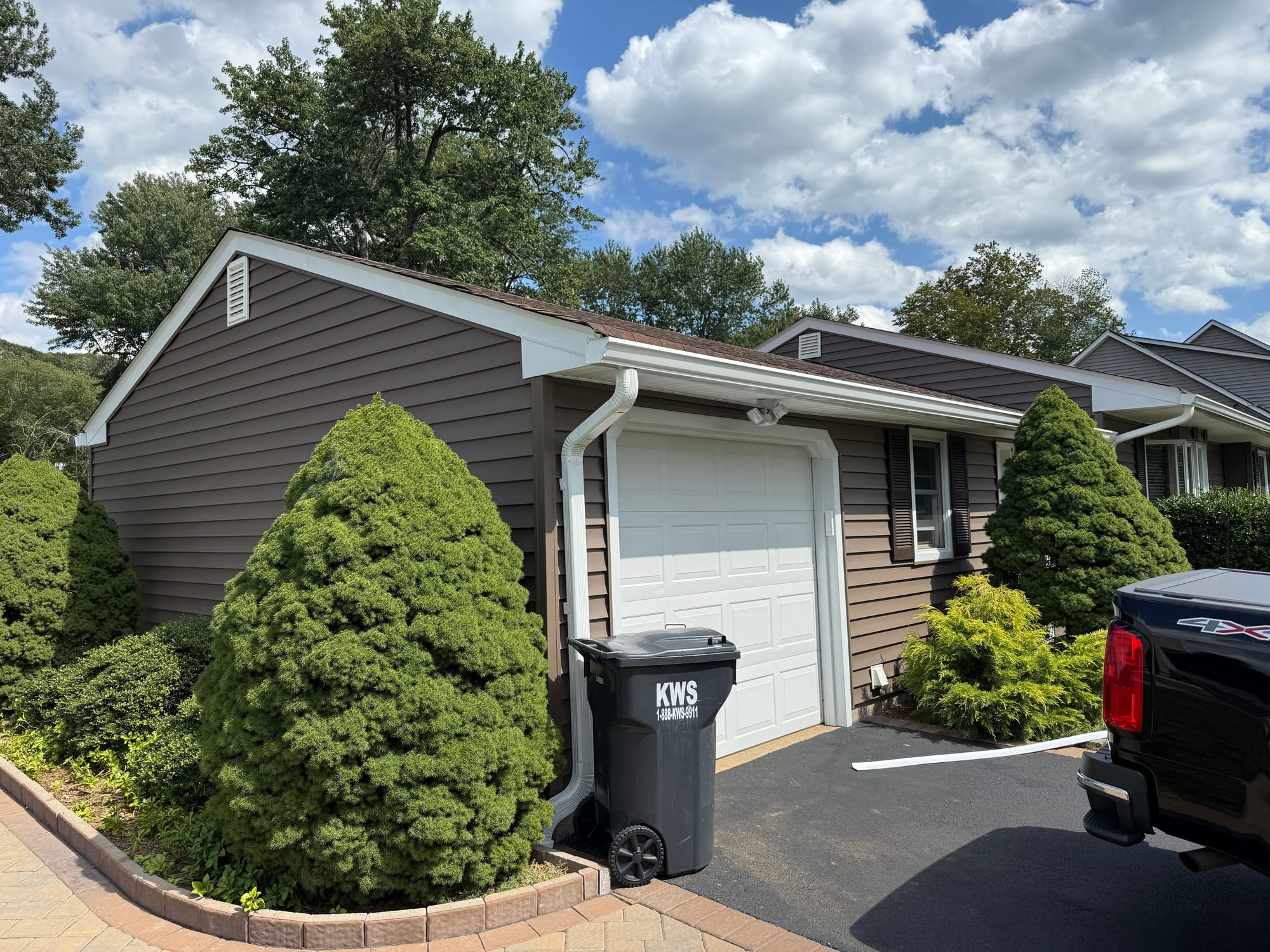 After: gable end and attached garage in clay-brown vinyl, cream corner posts and rake trim, new white downspout