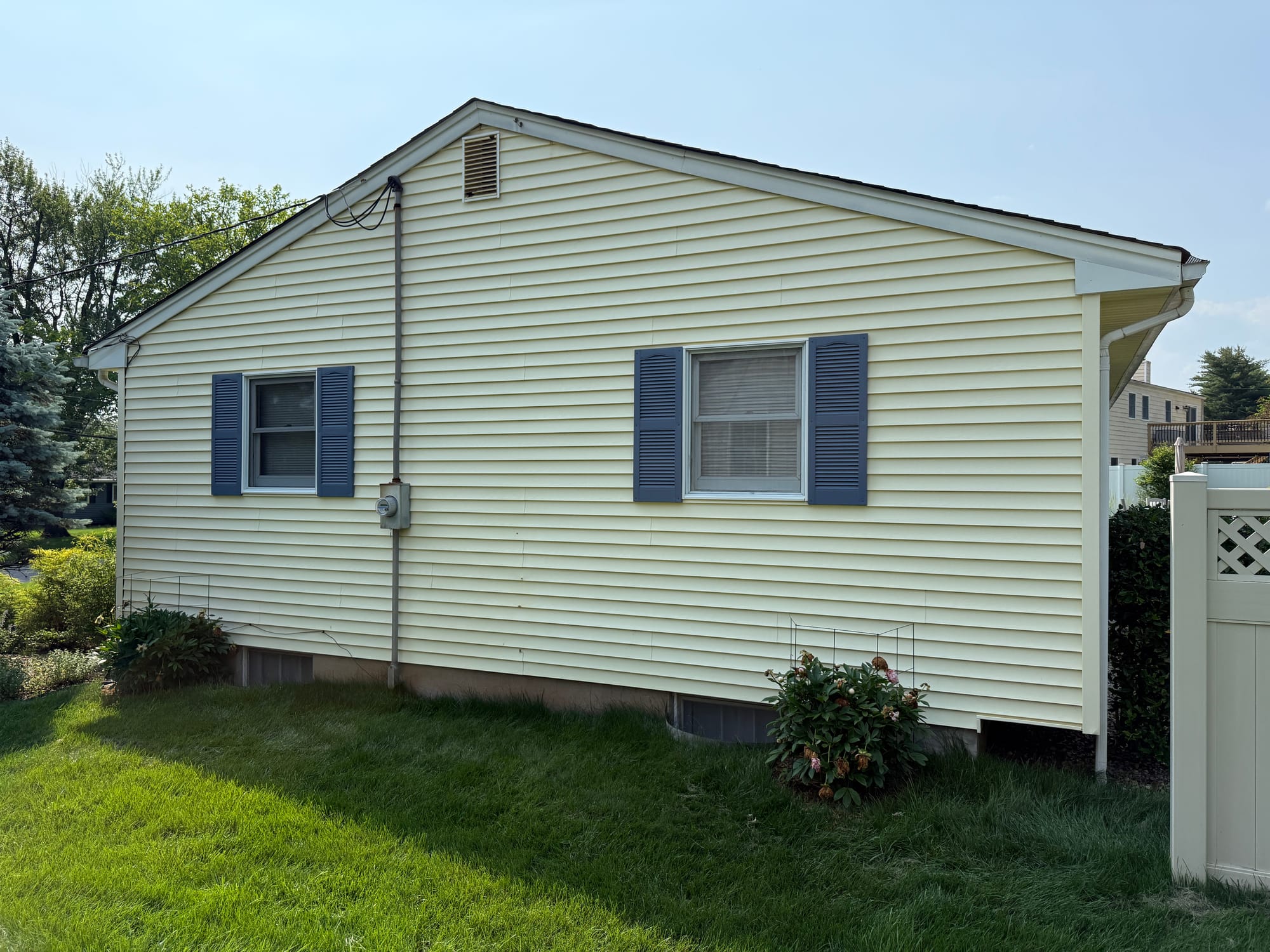 Before: side elevation in original yellow vinyl, blue shutters, white vinyl fence beyond
