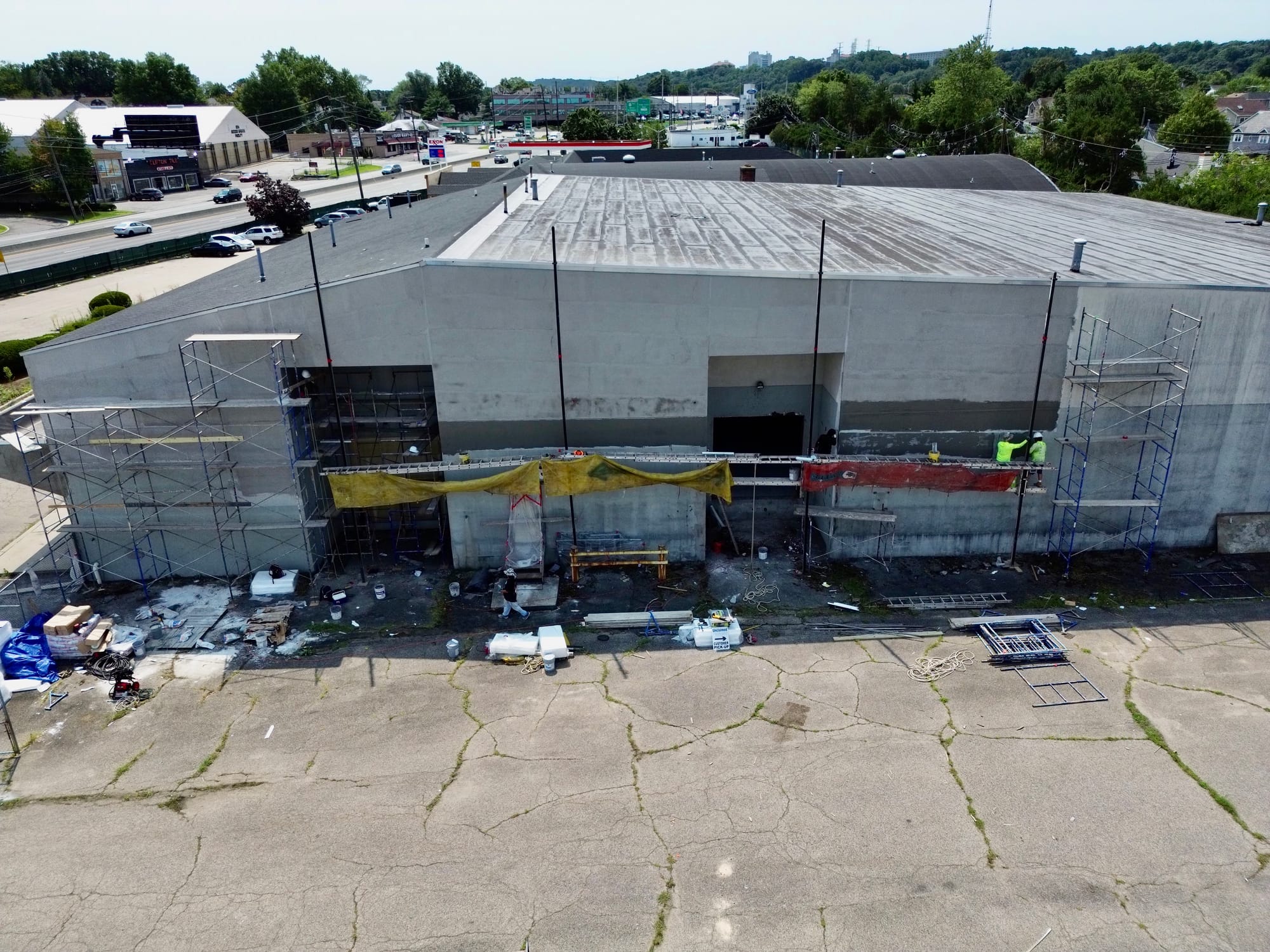 Scaffold across the full front elevation of a Clifton, NJ retail building, crews working the wall and materials staged on the forecourt
