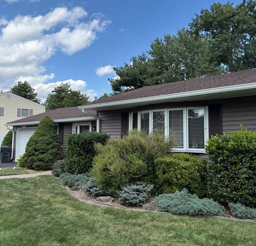 The front elevation of a house in Bridgewater after re-siding. New dark siding and white trim run across the elevation behind mature foundation planting, with a white bay window at the center.