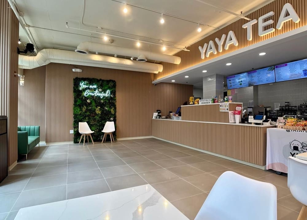 Finished cafe interior in Newark. A long service counter in pale stone and vertical timber slats runs down the right side under illuminated menu boards, with a preserved-plant living wall and lounge seating at the far end of the tiled floor.