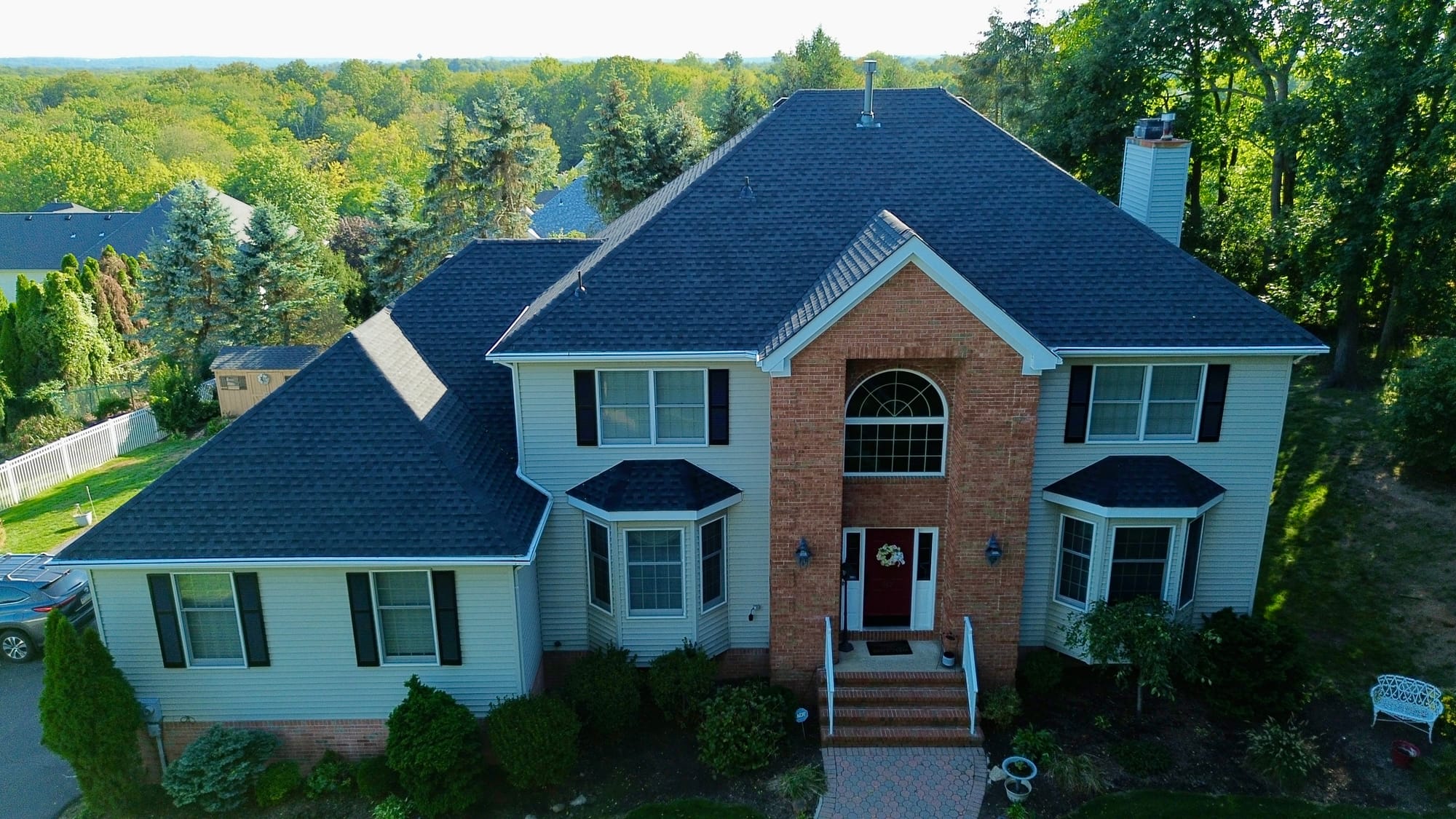After: front elevation from the air, new charcoal architectural shingle over the brick portico and bay windows