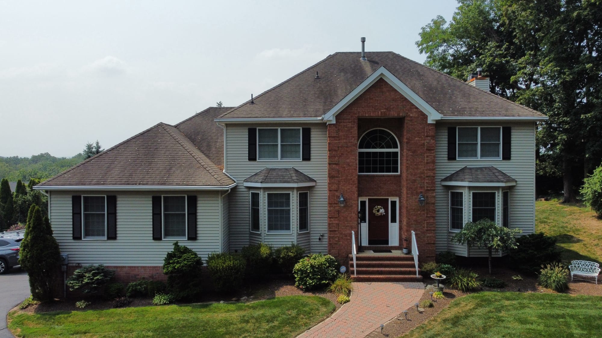 Before: front elevation from the air, original tan shingle heavily streaked and worn across the main hips