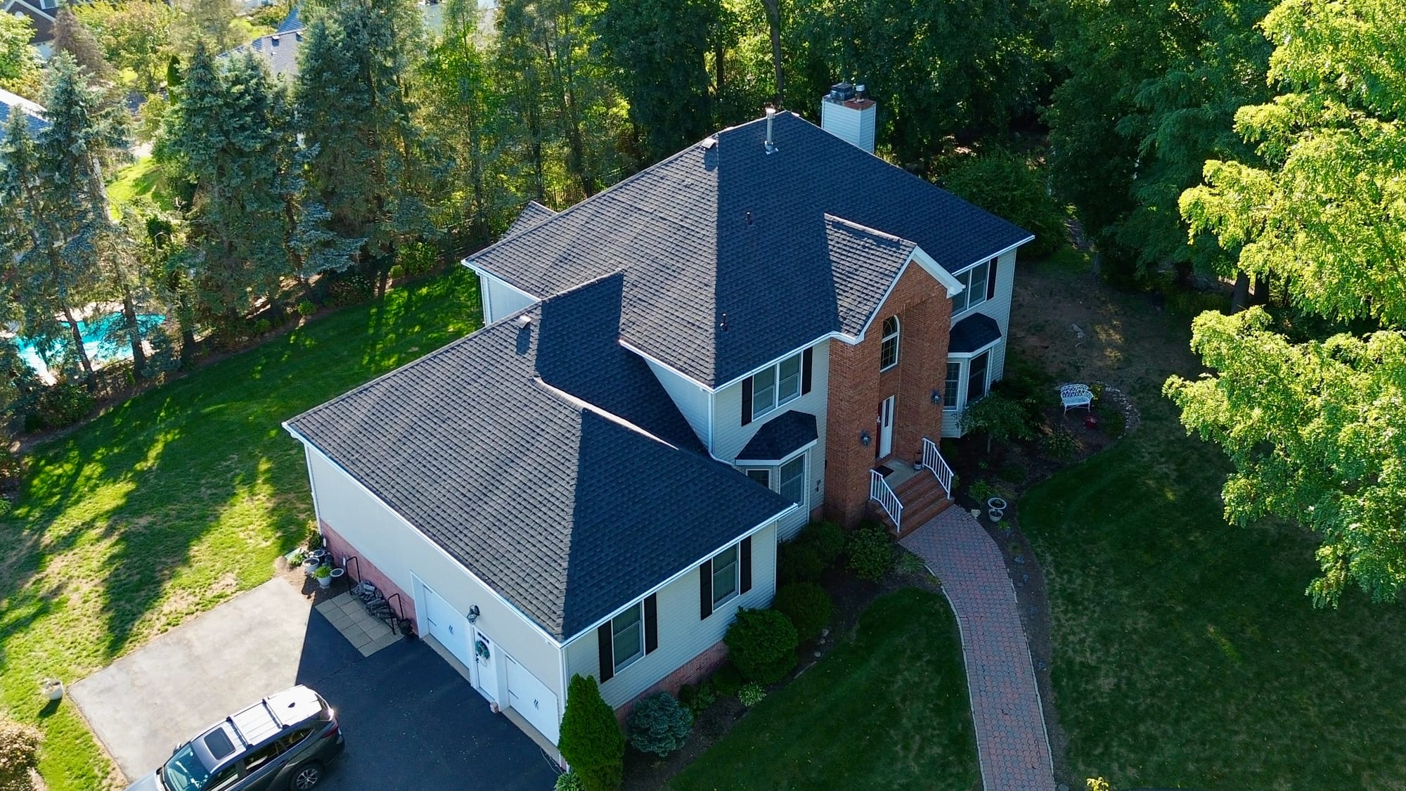 After: front-quarter aerial, new roof reading uniform across the main hip, dormers and garage wing