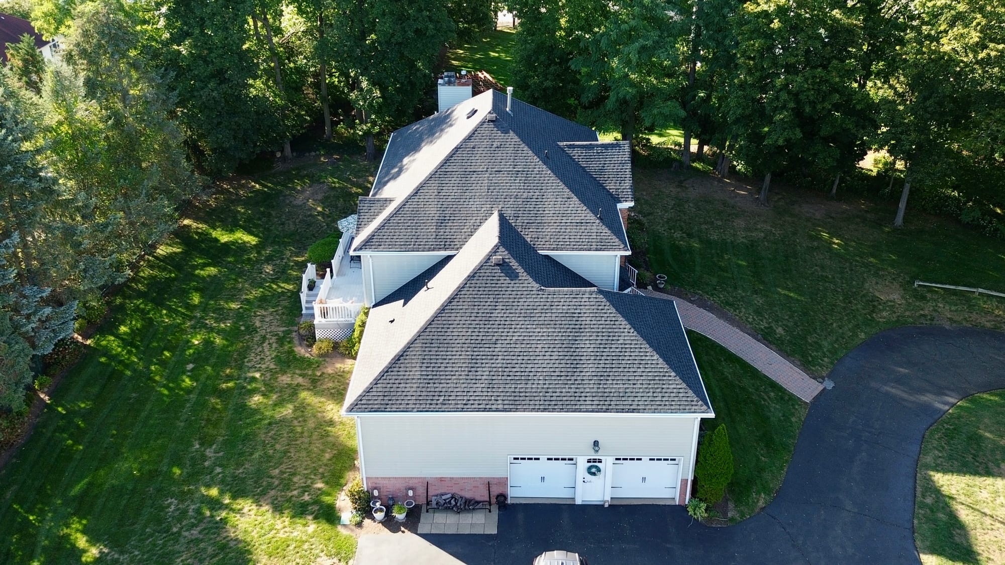 After: rear-quarter aerial over the deck, new shingle carried across the rear hips and the garage roof