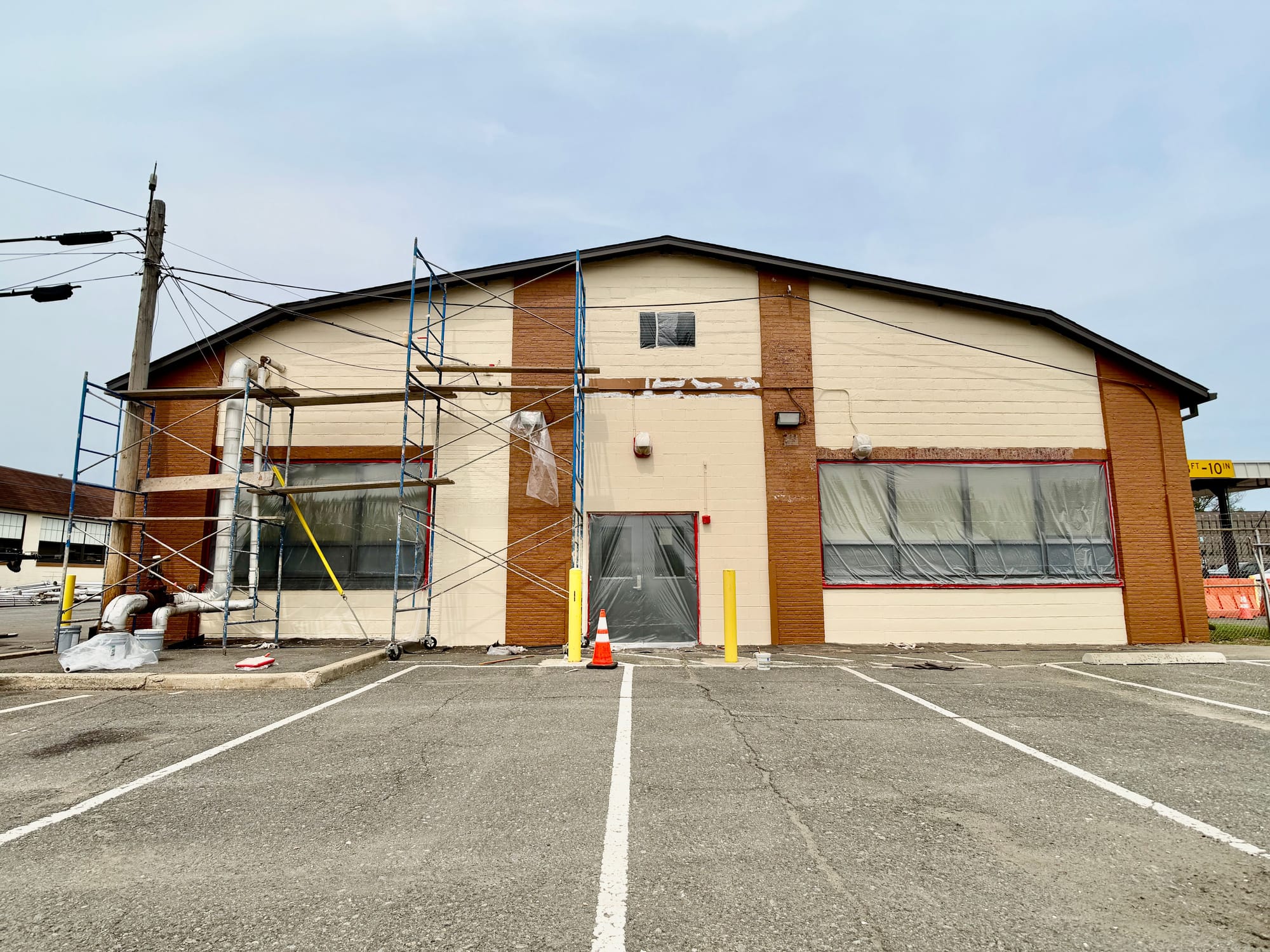 During: the same front elevation with scaffold up, windows and entry doors masked off and sealant repairs running across the block field