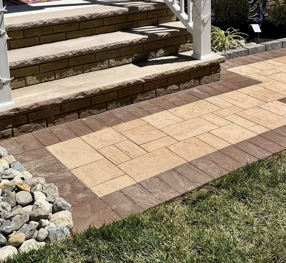 Approach to the porch, the paver field and its border reading square against the front steps and the stone bed