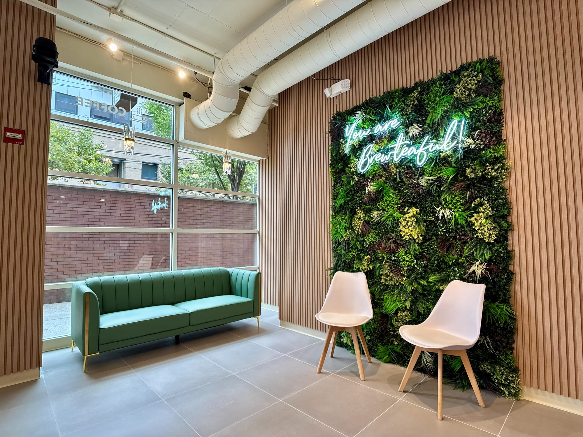 Preserved-plant living wall with neon script, green sofa and two chairs in the window lounge