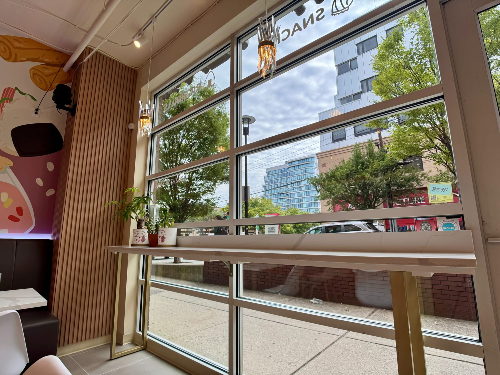 Timber counter-height rail seating at the shopfront glazing, mural returning onto the left wall